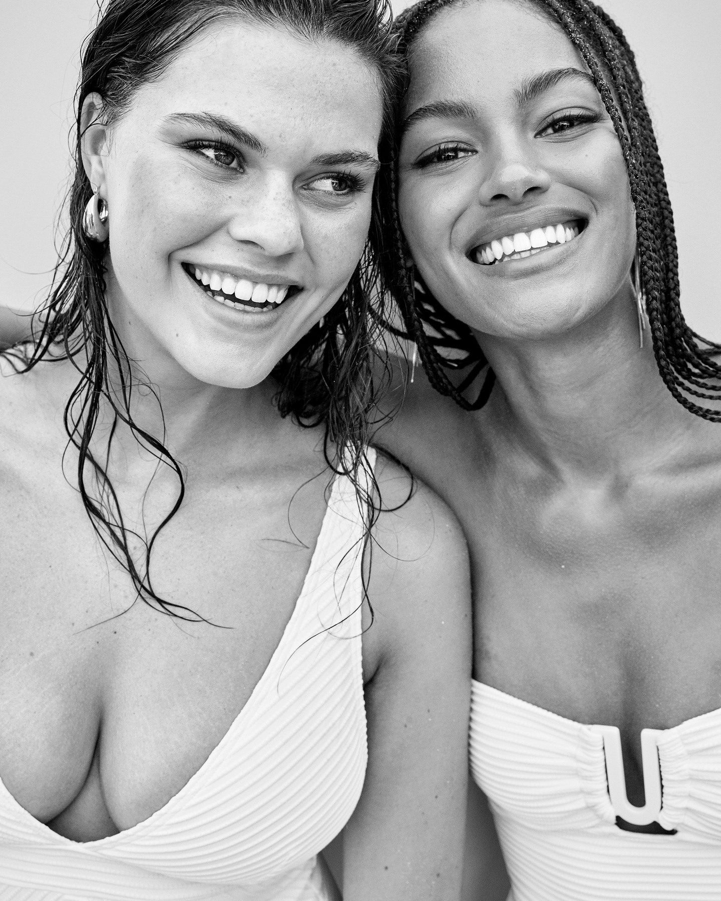 Black-and-white portrait of two smiling women in swimwear. One woman has dark hair and the other has braided hair. Close-up shot.