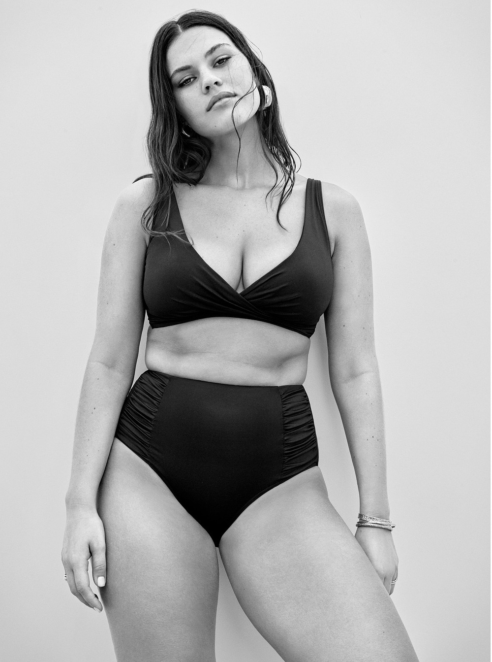 A woman poses in a high-waisted bikini set against a plain backdrop, creating a classic swimwear fashion shot in black and white.