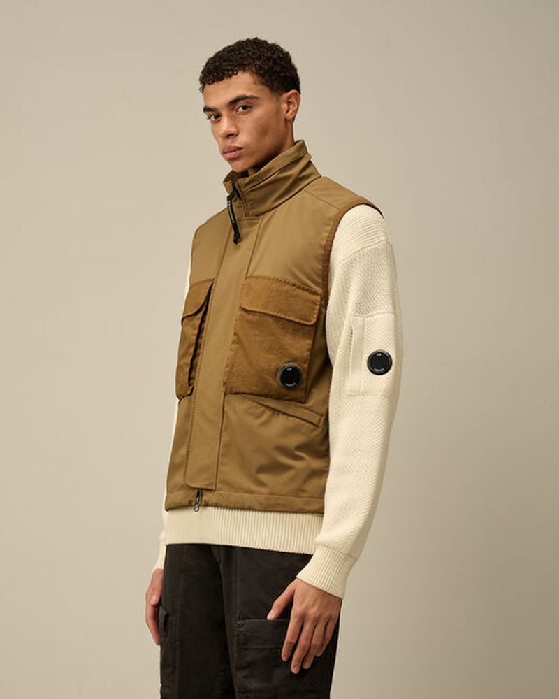 Man wearing a brown vest and white knit sweater in a studio setting, showcasing fashion apparel against a neutral background.
