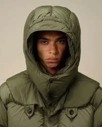 Man wearing an olive green hooded puffer jacket against a neutral studio background for C.P. Company