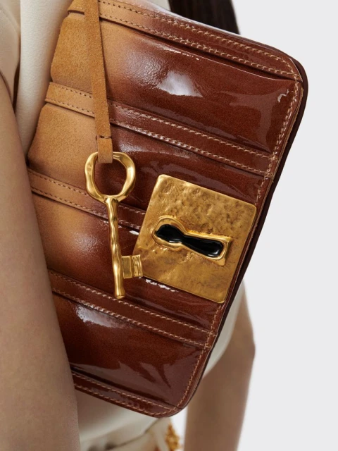 Close-up of a brown leather clutch with gold hardware and a decorative key, against a neutral background.