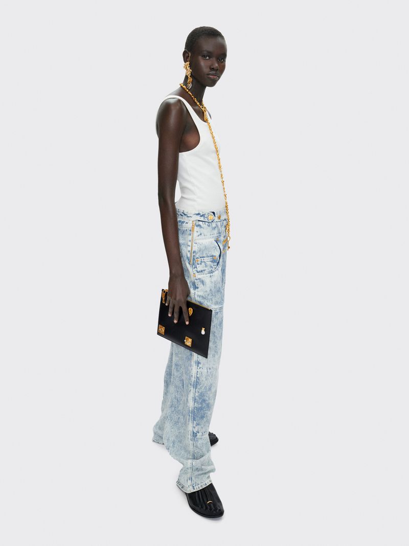 Profile shot of a woman in white tank top and acid wash jeans, holding a black clutch against a neutral background, accessorized with gold jewelry.
