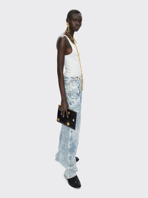 Profile shot of a woman in white tank top and acid wash jeans, holding a black clutch against a neutral background, accessorized with gold jewelry.