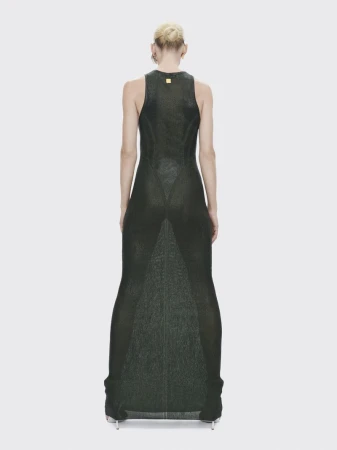 Back view of an adult female fashion model wearing a green, sleeveless, floor-length dress against a white backdrop in a studio.