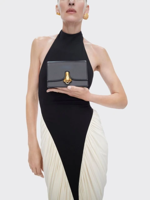 Woman in black and white dress holding a small black purse with gold hardware against a neutral background in a studio setting.