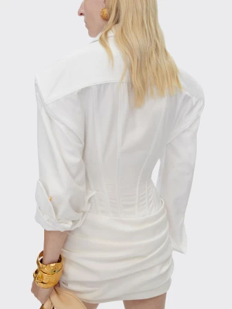 Woman wearing white blouse and skirt, gold bracelet and earring with light skin, shot from behind in front of white background.