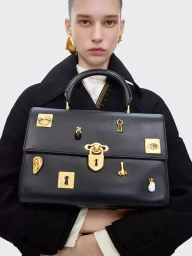 Model holding a black leather handbag adorned with ornate gold hardware against a plain white background.