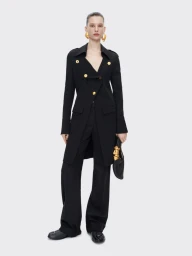 Model wearing a black coat with gold buttons, black trousers, and large gold earrings against a white background