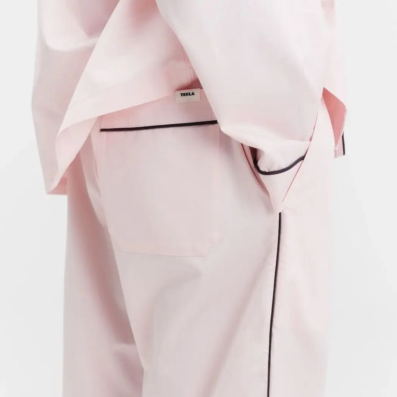 Close-up of a light pink pajama set with black piping. The top has a pocket with the brand label visible against a plain white background.