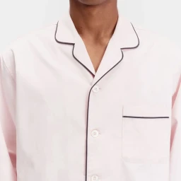 Close-up of a person wearing a light pink pajama shirt with contrast dark piping and white buttons against a white background.