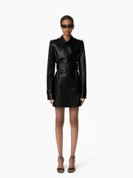 Model wearing a black belted coat and sunglasses standing against a plain white background