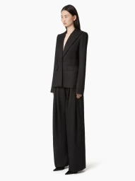Model wearing a black tailored blazer and matching trousers against a seamless white studio background