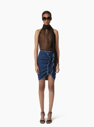Model wearing dark sunglasses, sheer black halter top, and blue denim skirt with ruffle detail against a plain background