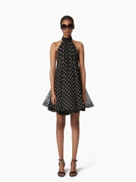 Model in dark sunglasses wearing a black halter dress with white polka dots against a white background