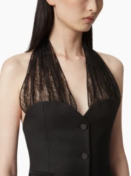 Close-up of a model wearing a black halter-neck top with sheer lace details and dark buttons against a plain white background.