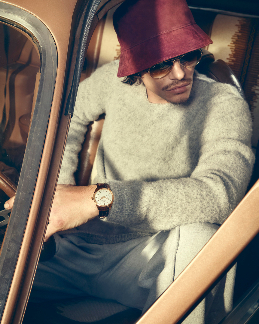 Man in car wearing sunglasses and a hat. The image showcases an adult male in casual attire inside an older car model with a focus on fashion.