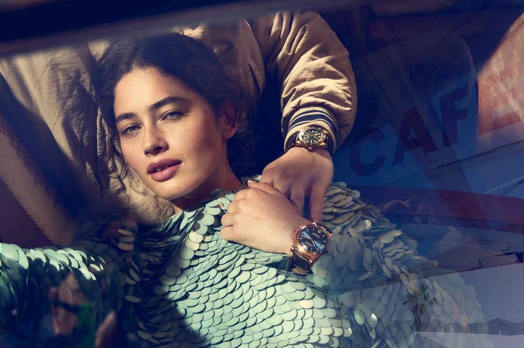 Glamorous woman in an iridescent dress with two watches being modeled, shot with natural light, indoor setting. Fashion and beauty shoot.
