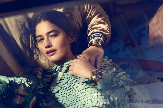 Glamorous woman in an iridescent dress with two watches being modeled, shot with natural light, indoor setting. Fashion and beauty shoot.