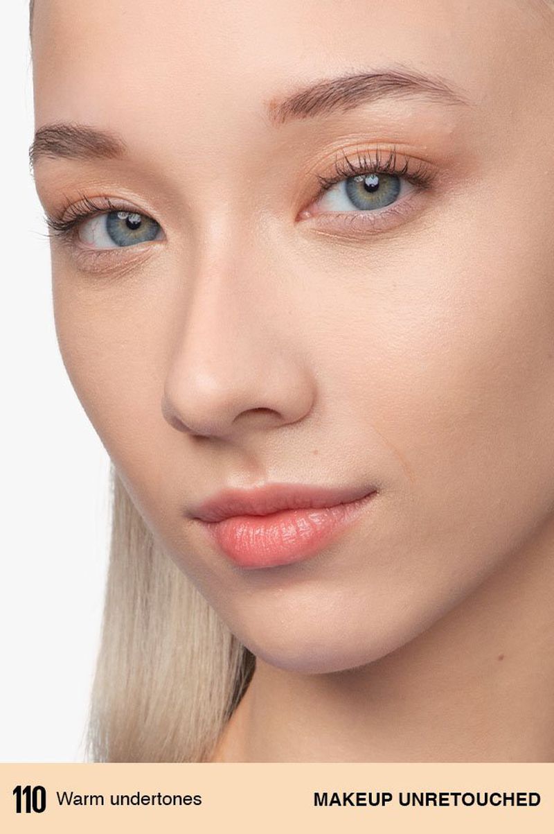 Close-up portrait of a young adult woman with light skin and blue eyes, featuring a foundation makeup application.
