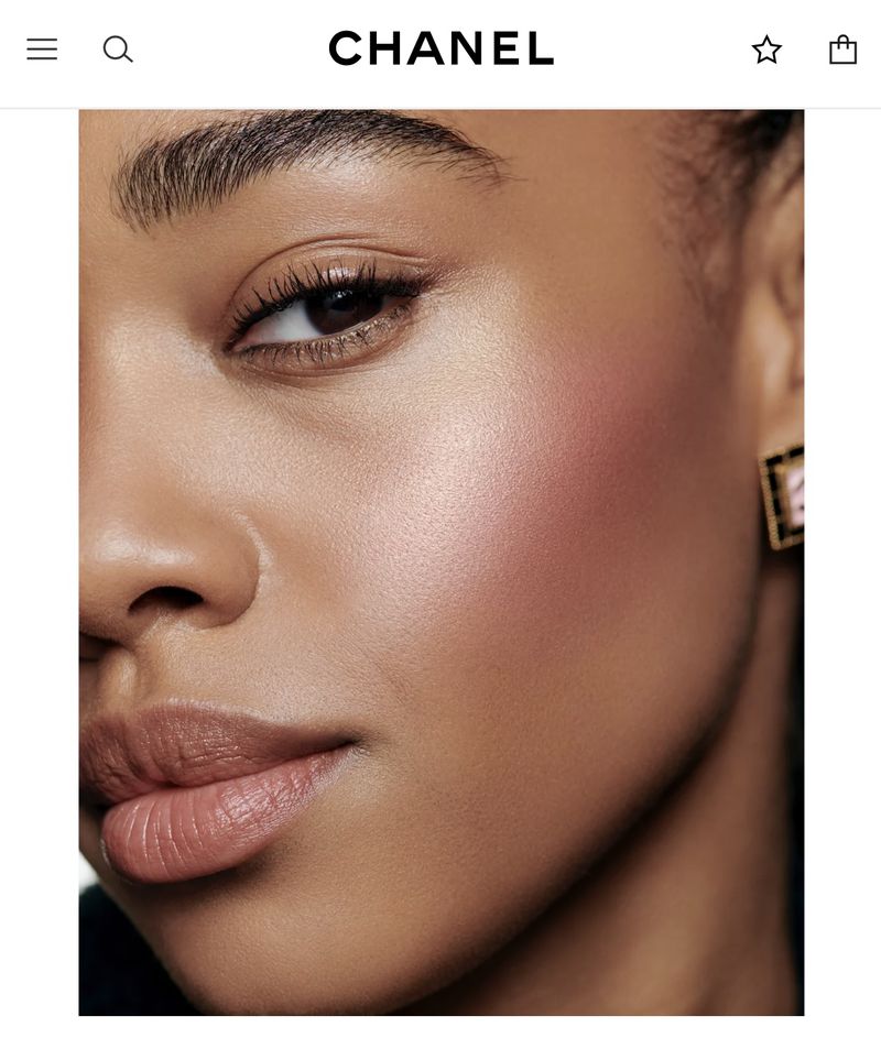 Close-up of a woman's face with tan skin wearing blush. A square earring with pink detail is visible. Beauty shot for makeup advertisement.