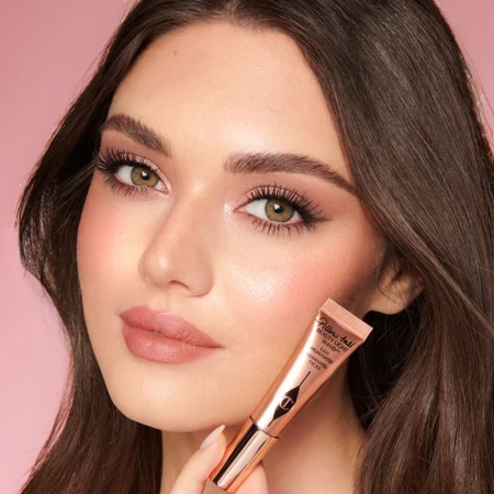 Close-up of woman holding beauty product, Charlotte Tilbury Pillow Talk Beauty Light Wand, in studio with pink background.