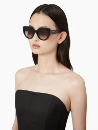 Model wearing black sunglasses and a black strapless top against a white seamless background for Nina Ricci