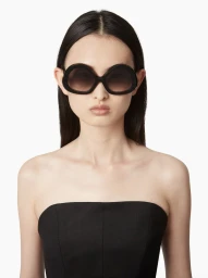 Model wearing oversized black sunglasses and a strapless black top against a plain white background for Nina Ricci.