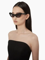 Model wearing black cat-eye sunglasses and a strapless black top against a solid white background
