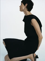 Model kneeling in a black sleeveless dress against a white studio background for Arket women ecom project