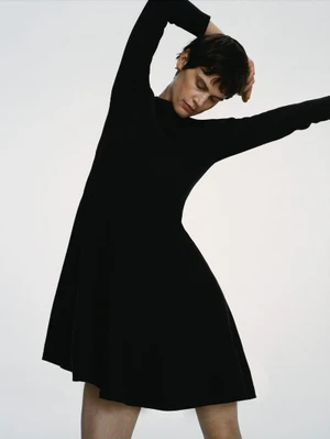 Model in a black long-sleeved dress posing against a plain white background for Arket women ecom