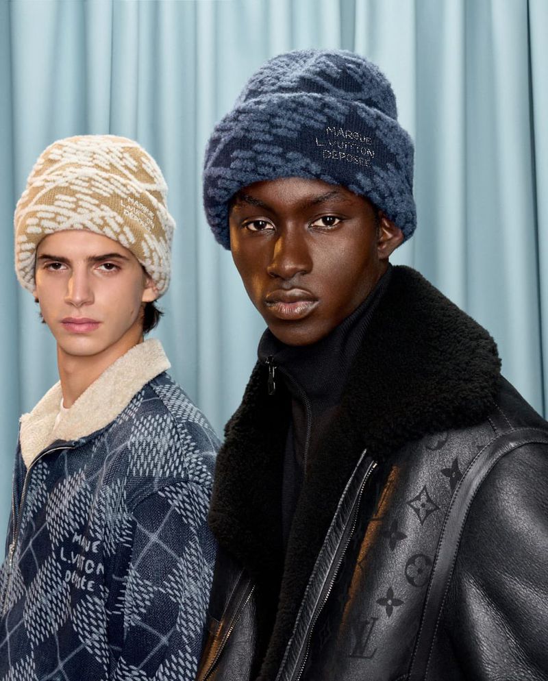 Two fashion models wearing beanies and jackets. One model wears a brown beanie and jacket, the other wears a blue beanie and jacket.