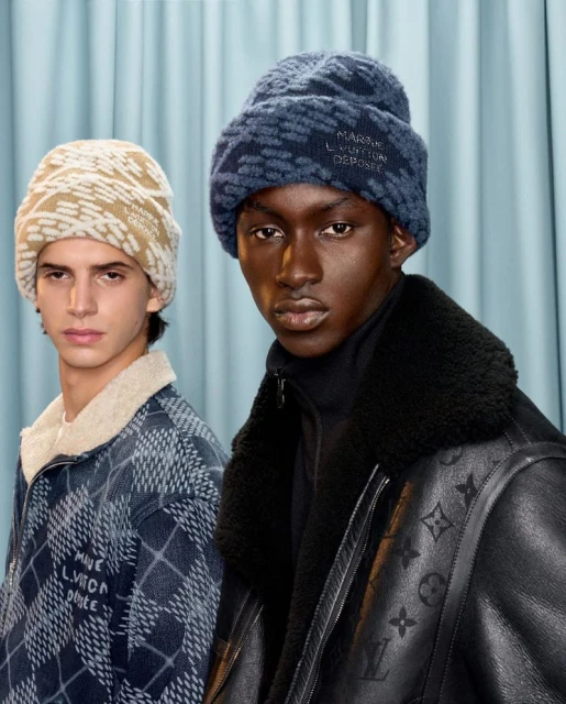 Two fashion models wearing beanies and jackets. One model wears a brown beanie and jacket, the other wears a blue beanie and jacket.