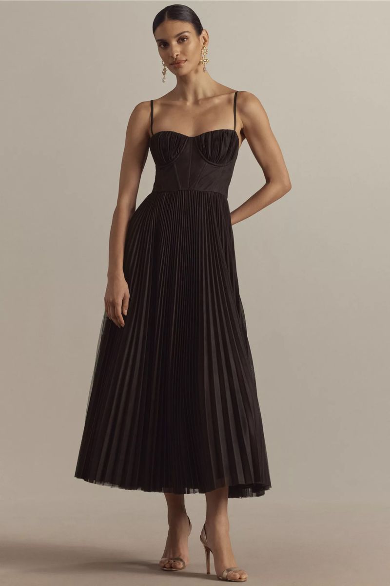 Elegant woman in a black pleated dress and heels. Indoor shot with neutral background. Fashion shoot showcasing formal wear.