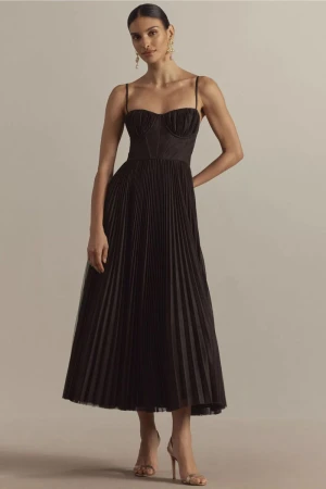 Elegant woman in a black pleated dress and heels. Indoor shot with neutral background. Fashion shoot showcasing formal wear.