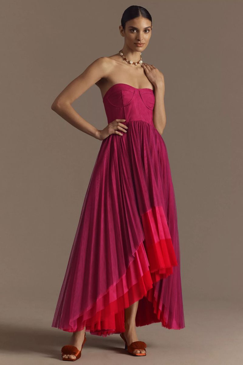 Elegant woman in a strapless fuchsia tulle dress with an asymmetrical hem posing in a studio with her hand on her hip.