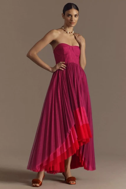 Elegant woman in a strapless fuchsia tulle dress with an asymmetrical hem posing in a studio with her hand on her hip.