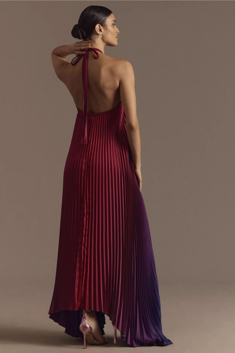Elegant woman from behind wearing a pleated halter gown transitioning from red to purple with stiletto heels in a studio setting.