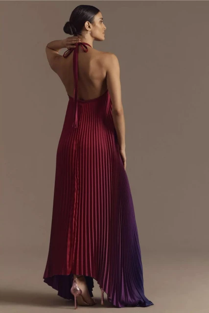 Elegant woman from behind wearing a pleated halter gown transitioning from red to purple with stiletto heels in a studio setting.