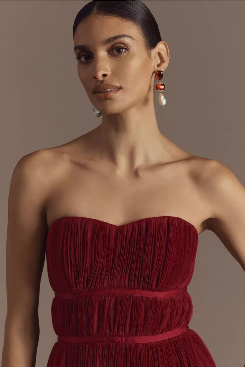 Elegant brunette woman in strapless burgundy dress with earrings poses in a close-up shot, showcasing fashion and beauty.