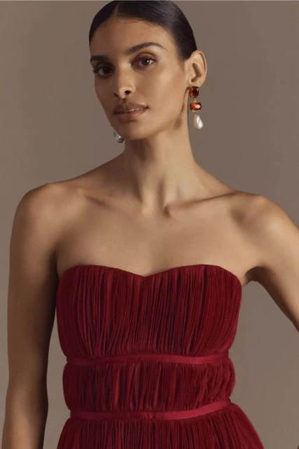 Elegant brunette woman in strapless burgundy dress with earrings poses in a close-up shot, showcasing fashion and beauty.