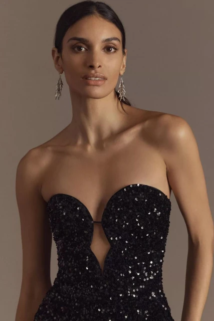 Elegant woman in a strapless black sequin gown poses in a studio setting, showcasing fashion and beauty elements.