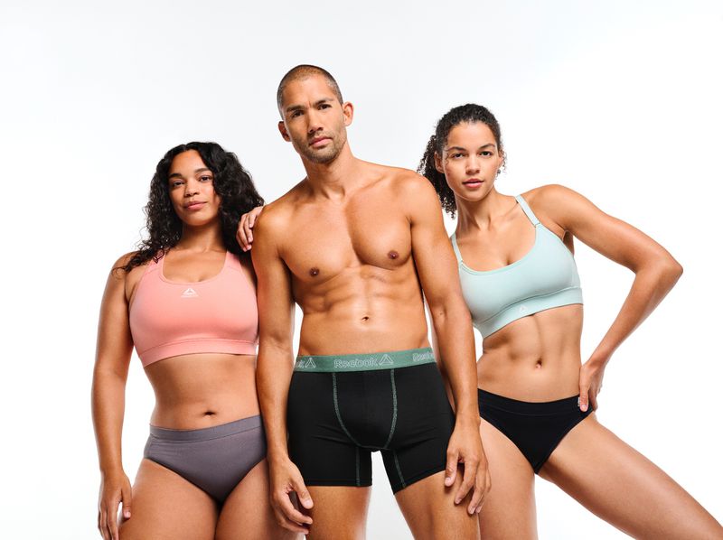 Three athletic people wearing underwear and sports bras in a brightly lit studio. Man in the center, women to either side. Fashion shot.