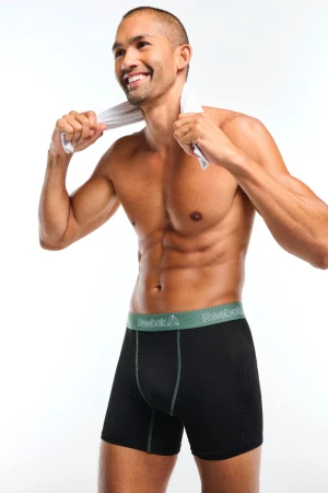 Athletic mixed-race man in underwear holds white towel on shoulders in studio, smiling. Fashion, fitness, and men's underwear product shot.
