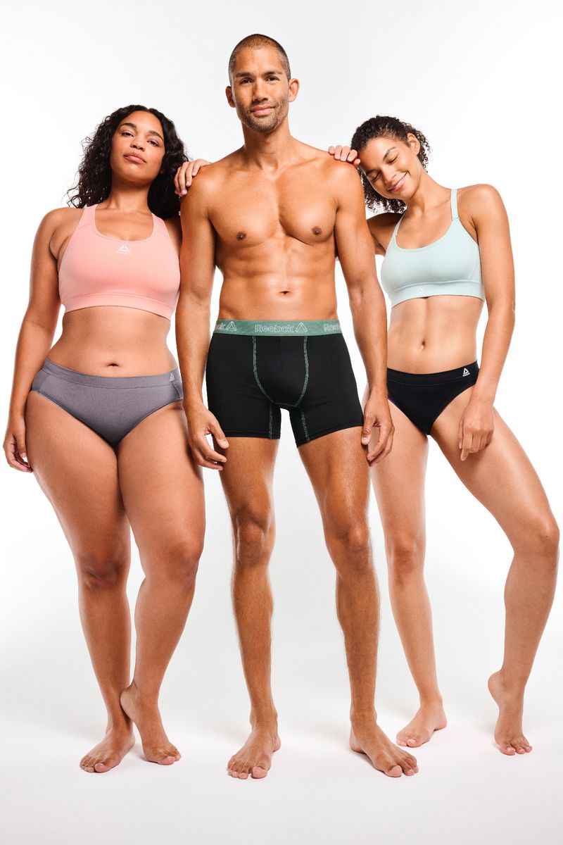 Three diverse adults pose in underwear and sports bras against a white backdrop in a studio shot promoting body positivity and comfort.