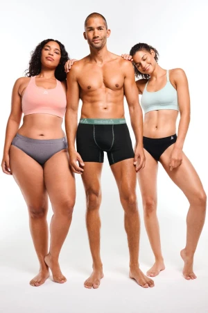 Three diverse adults pose in underwear and sports bras against a white backdrop in a studio shot promoting body positivity and comfort.