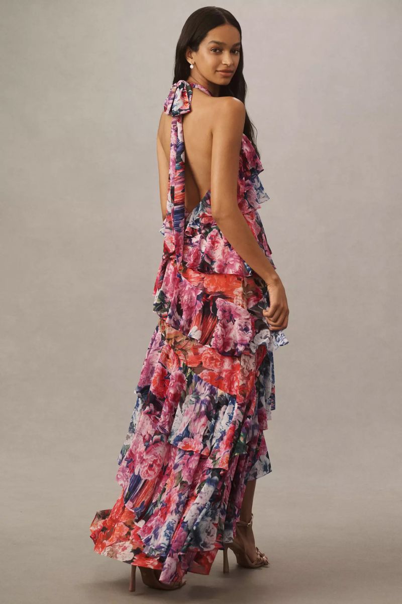 Elegant adult woman poses in a studio wearing a floral-patterned halter gown with tiered ruffles and high heels in a full shot.