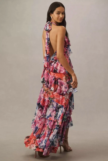 Elegant adult woman poses in a studio wearing a floral-patterned halter gown with tiered ruffles and high heels in a full shot.