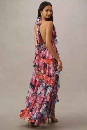 Elegant adult woman poses in a studio wearing a floral-patterned halter gown with tiered ruffles and high heels in a full shot.