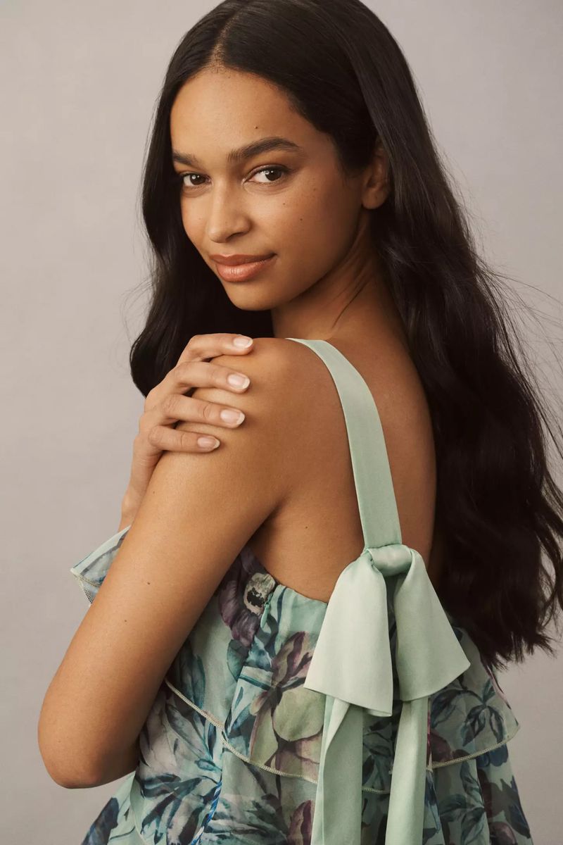 Portrait of a young adult female model with long dark hair, light skin, and a floral print top with ribbon straps, looking at the camera.