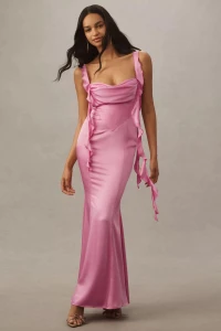 Model in a pink satin gown with ruffled straps standing against a neutral grey studio background